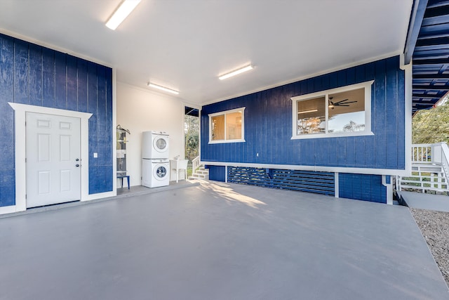 garage featuring wood walls, stacked washer and dryer, and water heater