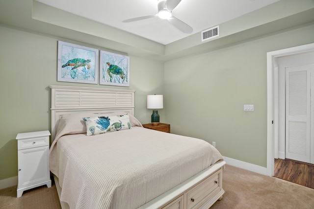 carpeted bedroom featuring a closet, ceiling fan, and a tray ceiling