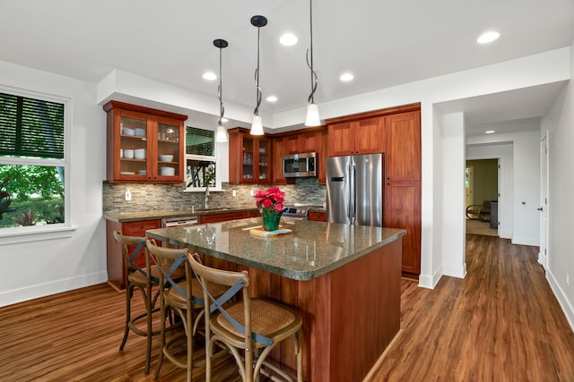 kitchen with hanging light fixtures, stainless steel appliances, dark hardwood / wood-style floors, dark stone counters, and a kitchen island