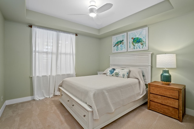 carpeted bedroom with ceiling fan and a tray ceiling