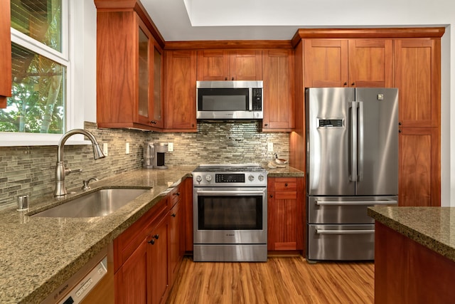 kitchen featuring decorative backsplash, light stone countertops, light wood-type flooring, stainless steel appliances, and sink