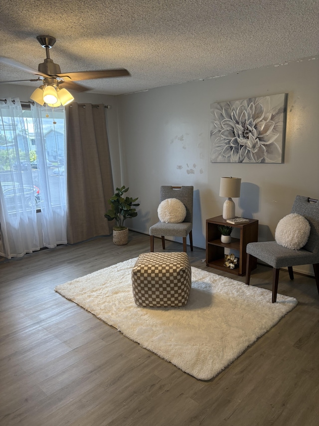 living area with ceiling fan, wood-type flooring, and a textured ceiling