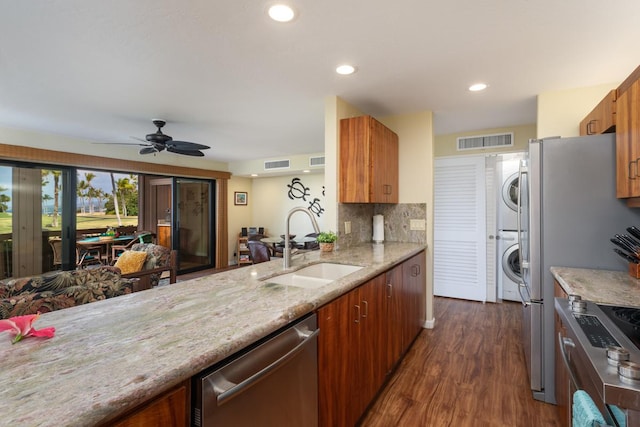 kitchen with appliances with stainless steel finishes, dark hardwood / wood-style flooring, ceiling fan, sink, and stacked washer and dryer