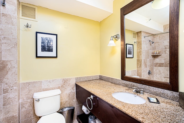 bathroom with vanity, toilet, tile walls, and a tile shower