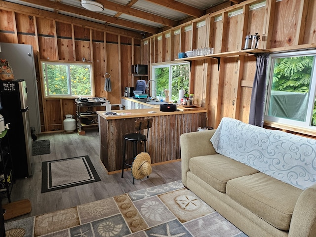 interior space with a breakfast bar, beam ceiling, dark hardwood / wood-style flooring, kitchen peninsula, and stainless steel refrigerator