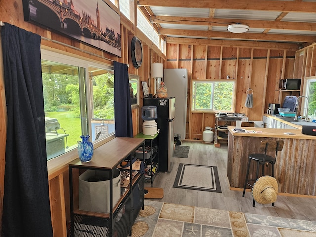 kitchen with sink, wooden walls, light hardwood / wood-style flooring, beam ceiling, and stainless steel refrigerator