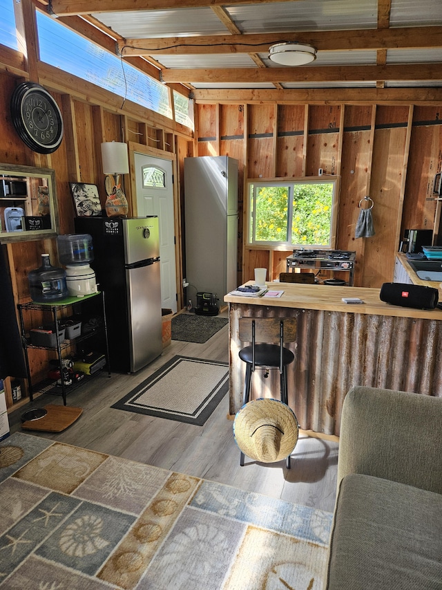 kitchen featuring hardwood / wood-style floors, stainless steel refrigerator, beam ceiling, and wood walls