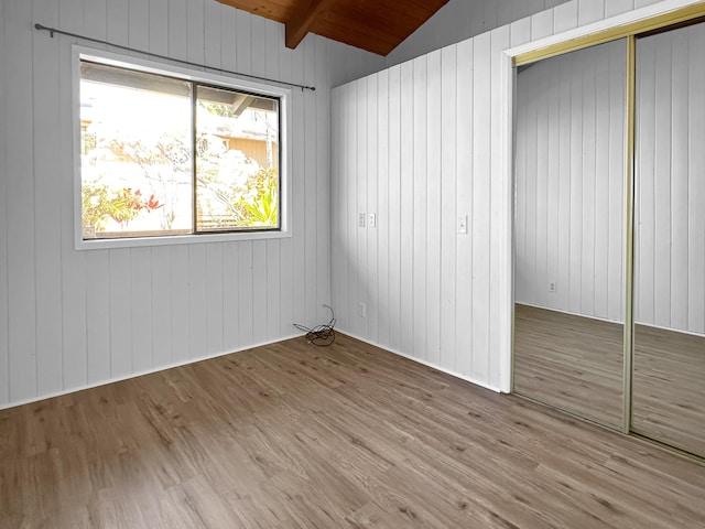 unfurnished bedroom with light hardwood / wood-style flooring, wooden ceiling, vaulted ceiling with beams, a closet, and wood walls