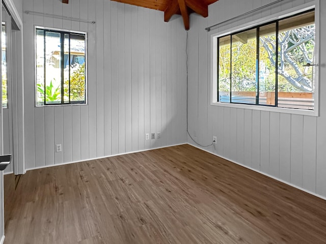 unfurnished room with beamed ceiling, wood walls, and wood-type flooring