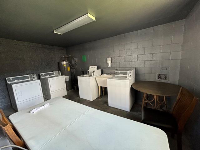 washroom featuring washing machine and dryer, laundry area, electric water heater, and concrete block wall