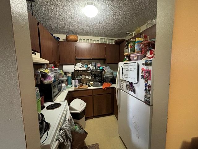 kitchen featuring white electric stove, a textured ceiling, under cabinet range hood, freestanding refrigerator, and stainless steel microwave