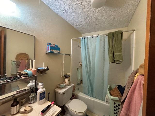 full bath with toilet, shower / bath combo, and a textured ceiling