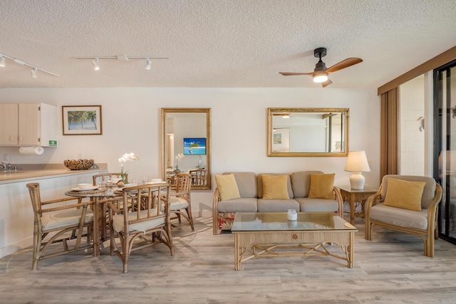 living room with ceiling fan, a textured ceiling, and light hardwood / wood-style flooring