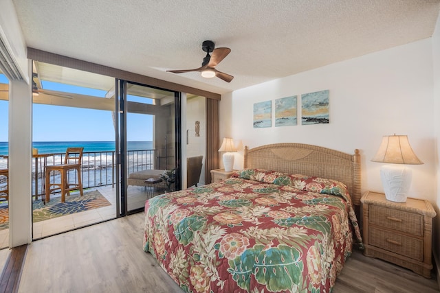 bedroom featuring ceiling fan, hardwood / wood-style floors, a textured ceiling, access to outside, and a water view