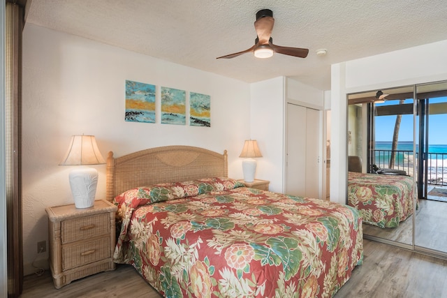 bedroom featuring a water view, light hardwood / wood-style flooring, ceiling fan, access to exterior, and a closet