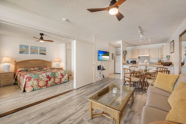 bedroom with a textured ceiling, white fridge, rail lighting, and light hardwood / wood-style floors