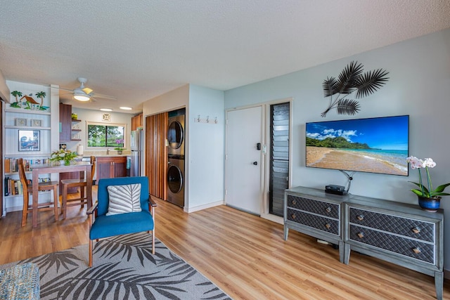 living room featuring a textured ceiling, light hardwood / wood-style floors, stacked washer / dryer, and ceiling fan