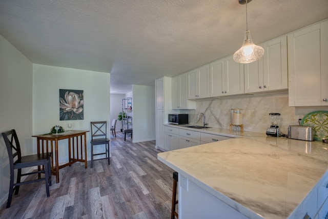 kitchen with backsplash, sink, pendant lighting, hardwood / wood-style flooring, and white cabinetry