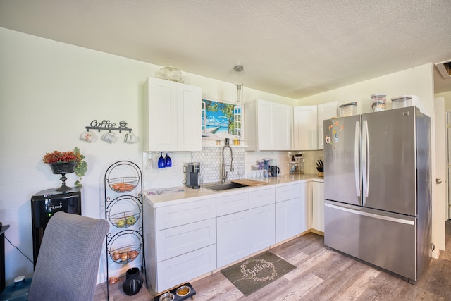 kitchen with sink, decorative backsplash, light wood-type flooring, white cabinetry, and stainless steel refrigerator