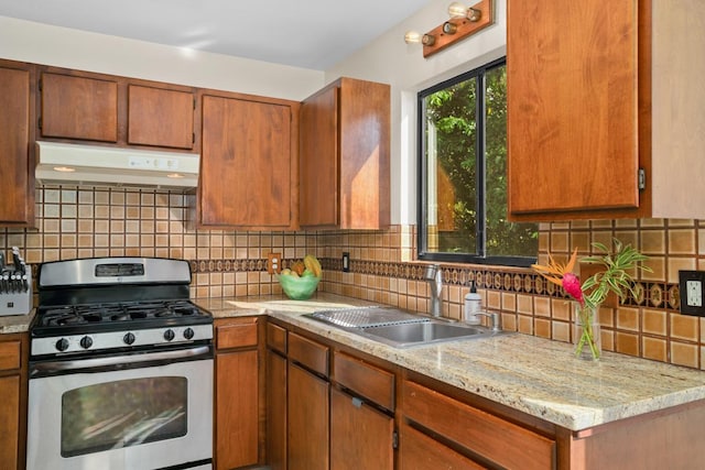 kitchen featuring stainless steel gas stove, light stone countertops, decorative backsplash, and sink