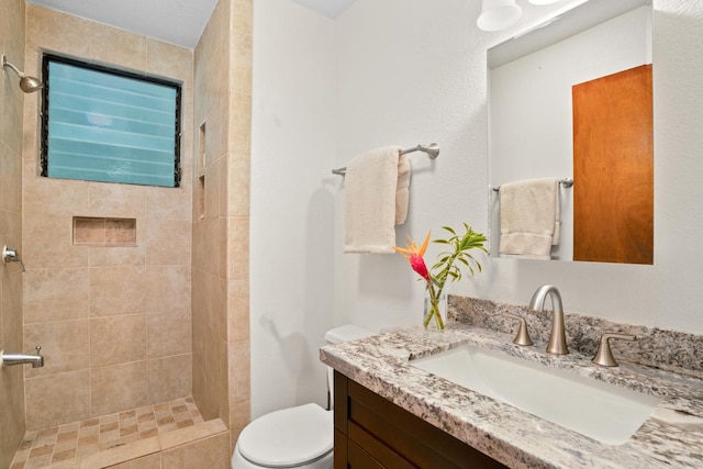 bathroom featuring toilet, vanity, and tiled shower