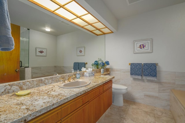 bathroom with vanity, a shower with door, tile patterned floors, toilet, and tile walls