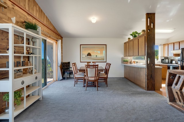 dining room with light carpet, vaulted ceiling, plenty of natural light, and wooden walls