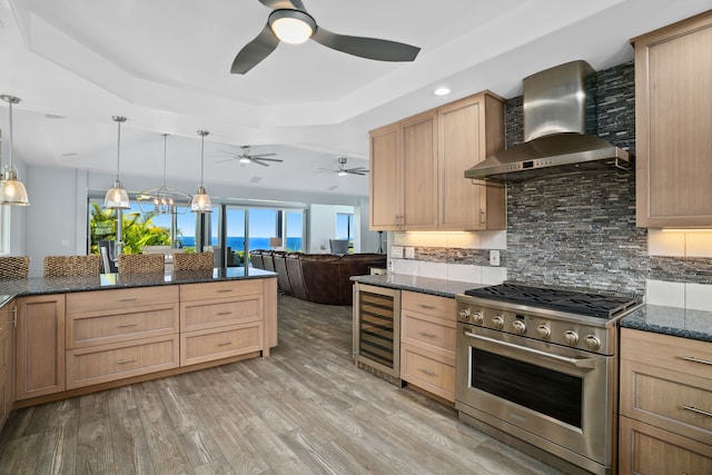 kitchen featuring wall chimney exhaust hood, beverage cooler, high end stove, light hardwood / wood-style floors, and pendant lighting