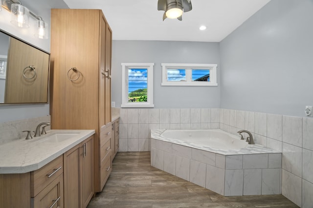 bathroom featuring vanity, a relaxing tiled tub, ceiling fan, tile walls, and wood-type flooring