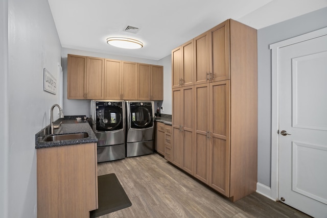 clothes washing area with cabinets, hardwood / wood-style flooring, washer and dryer, and sink