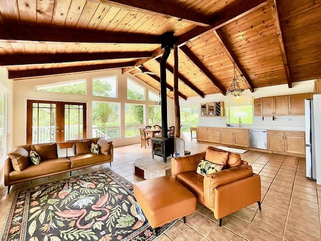 tiled living room featuring a wood stove, sink, lofted ceiling with beams, a notable chandelier, and wood ceiling