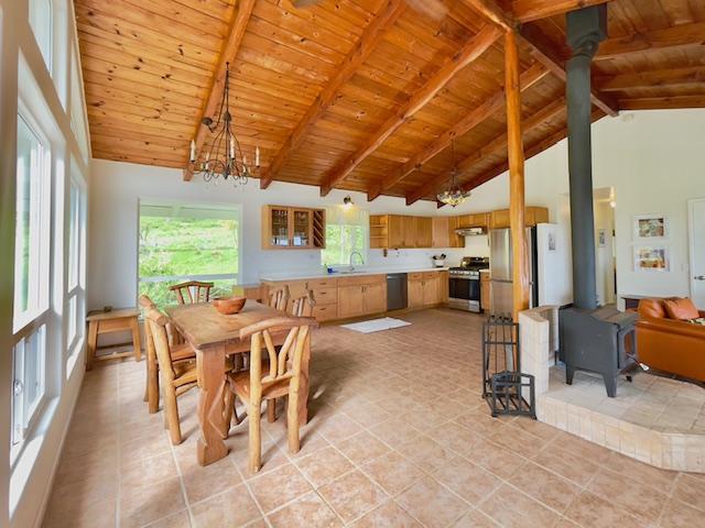 tiled dining space with beam ceiling, high vaulted ceiling, an inviting chandelier, wooden ceiling, and a wood stove