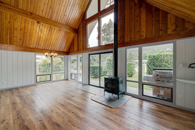 unfurnished sunroom with a healthy amount of sunlight, vaulted ceiling with beams, a wood stove, and a notable chandelier