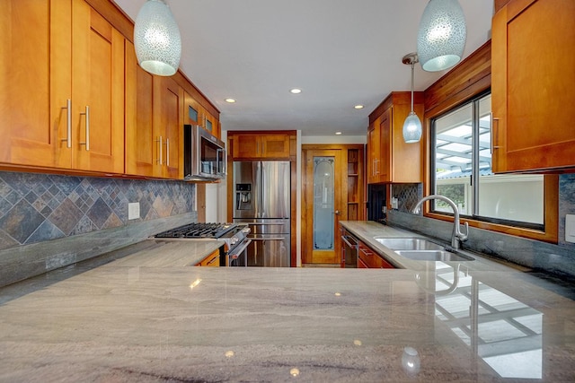 kitchen featuring light stone countertops, appliances with stainless steel finishes, decorative light fixtures, and sink