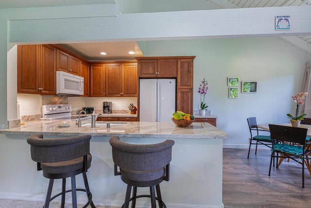 kitchen featuring kitchen peninsula, a kitchen breakfast bar, dark hardwood / wood-style flooring, light stone countertops, and white appliances