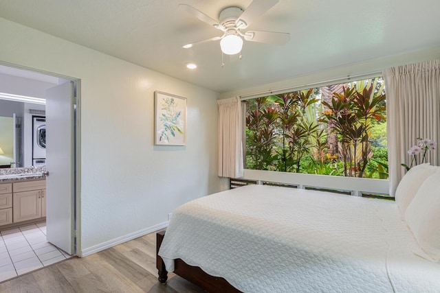 bedroom with connected bathroom, ceiling fan, stacked washer / drying machine, and light wood-type flooring