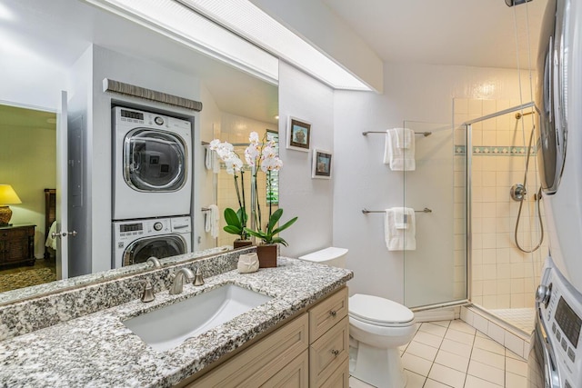 bathroom with stacked washing maching and dryer, tile patterned floors, an enclosed shower, vanity, and toilet