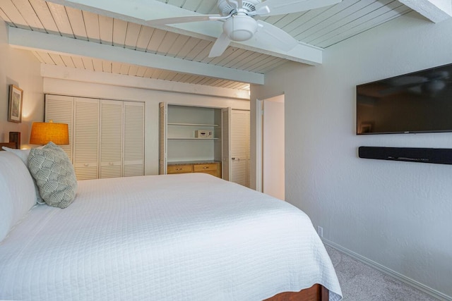 bedroom featuring beam ceiling, multiple closets, ceiling fan, and carpet flooring