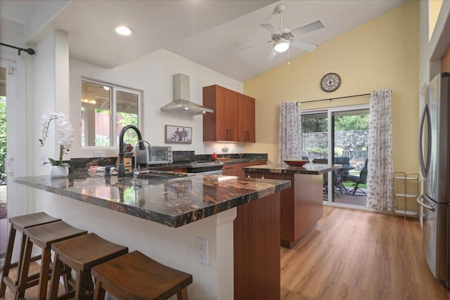 kitchen featuring a kitchen bar, wall chimney exhaust hood, light hardwood / wood-style floors, and appliances with stainless steel finishes