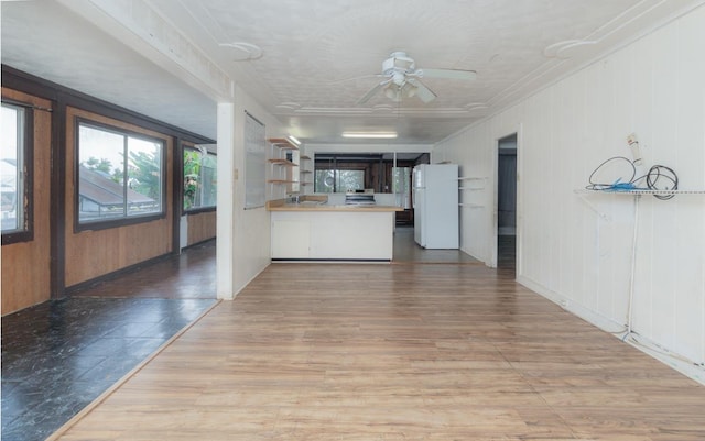 kitchen with kitchen peninsula, white fridge, wall chimney range hood, wooden walls, and ceiling fan