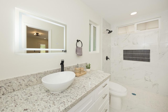 bathroom featuring a tile shower, vanity, and toilet