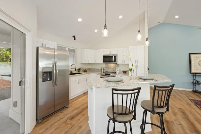 kitchen with appliances with stainless steel finishes, vaulted ceiling, sink, a center island, and white cabinetry