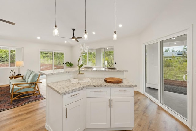 kitchen with light stone countertops, a kitchen island, pendant lighting, light hardwood / wood-style floors, and white cabinets