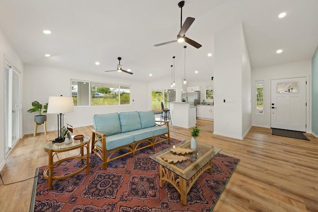 living room with ceiling fan, vaulted ceiling, and light wood-type flooring