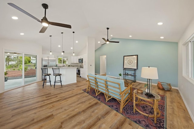 living room with ceiling fan, light wood-type flooring, and vaulted ceiling