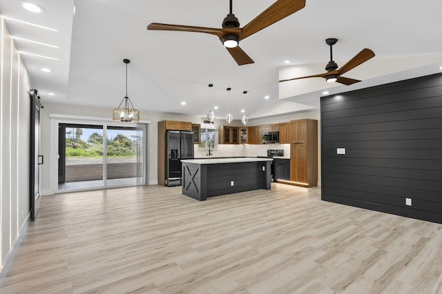 kitchen featuring black fridge with ice dispenser, a kitchen island, decorative light fixtures, and light wood-type flooring