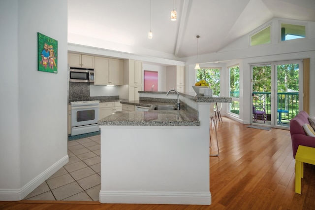 kitchen with pendant lighting, electric stove, sink, cream cabinetry, and light hardwood / wood-style floors