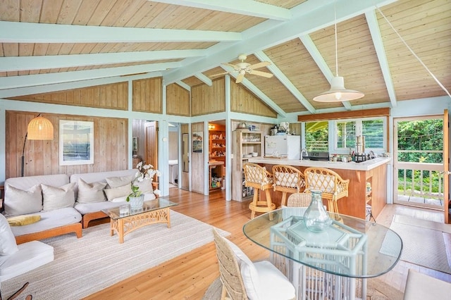 living room featuring ceiling fan, lofted ceiling with beams, wooden walls, wood ceiling, and light wood-type flooring