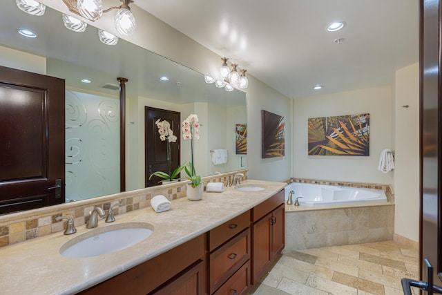 bathroom featuring vanity, an inviting chandelier, and tiled tub