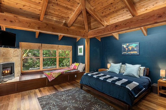 bedroom featuring hardwood / wood-style flooring, wood ceiling, beamed ceiling, and a tile fireplace